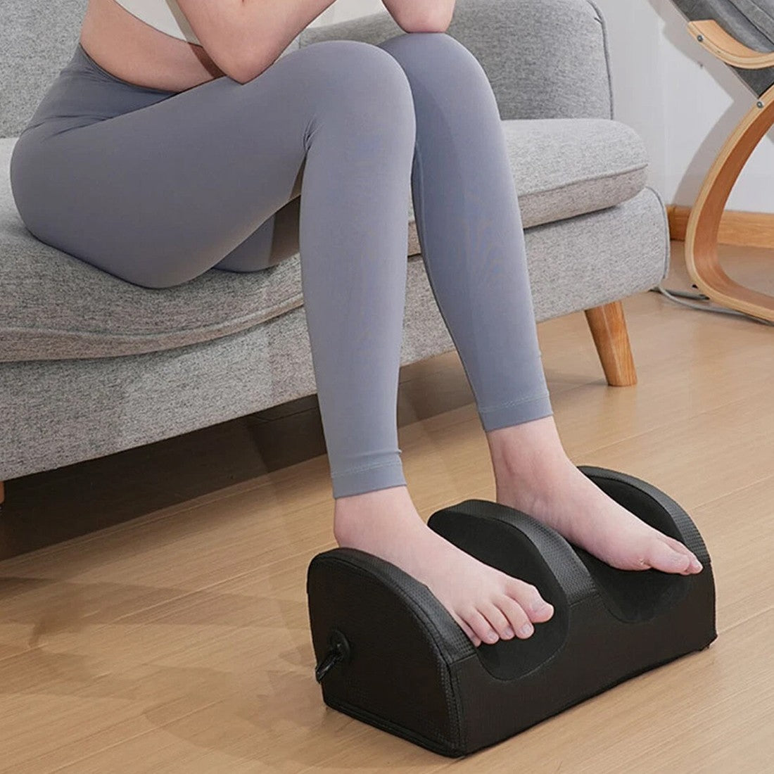Woman using NovaPulse foot massager for leg pain relief while sitting
